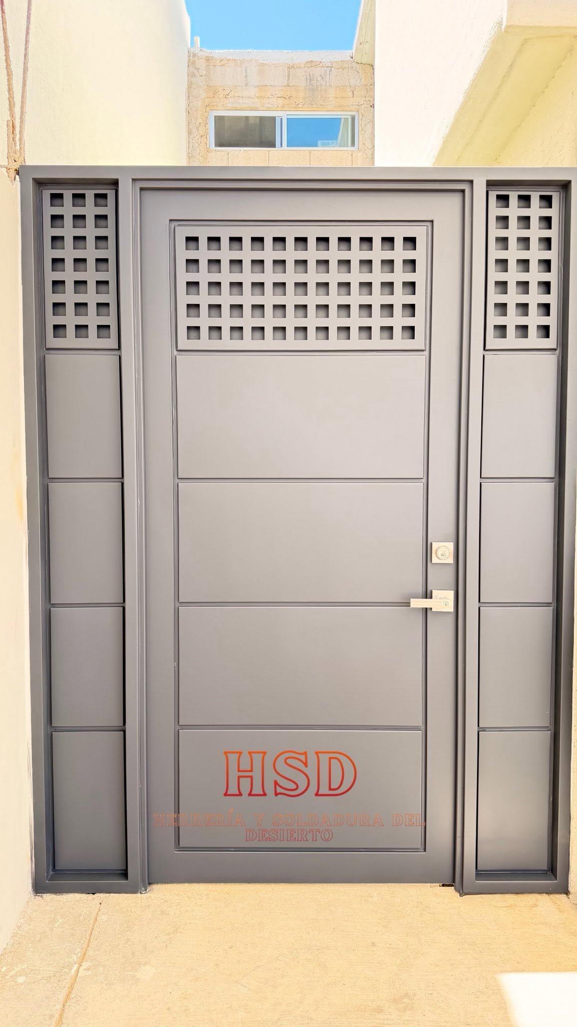 Puerta de acero gris con paneles horizontales, laterales fijos y celosía cuadriculada en la parte superior
